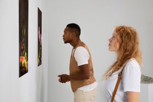 Two people closely examining a painting on a gallery wall.